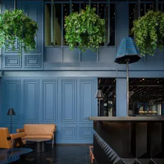 For this bar area, I created a cinematic, immersive mood using a deep blue palette on paneled walls and a faceted black granite bar. The design contrasts these cool, moody tones with the warmth of tan leather seating and a canopy of hanging plants, blending retro glamour with a touch of nature.