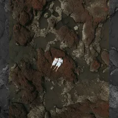 A breathtaking top-down drone photograph of a couple in white, finding a moment of peace on the rustic, rocky shores of Goa.