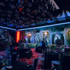 A wide view of a spectacular Sangeet setup. The ceiling is covered in disco balls, and the stage features ornate white arches and dramatic lighting, setting the stage for a night of music and dance.