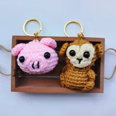 A clean product shot of the pig and monkey amigurumi keychains. They are the perfect size to hang on your keys or backpack without being too bulky.