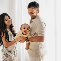 A bright and airy family portrait against a white curtained backdrop. The baby's happy expression is the centerpiece of this beautiful image.