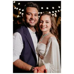 A close-up of the happy couple at their dinner event. Her modern white outfit and diamond jewelry pair beautifully with his tailored waistcoat, showing how contemporary looks can still feel special and celebratory.