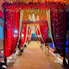 A classic and opulent entrance passage created with rich red and gold drapes. The path is lit by chandeliers and fairy lights, giving guests a royal welcome as they enter the celebration.