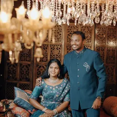 A formal portrait of a couple on a royal-themed set, her in a blue lehenga and him in a matching bandhgala.