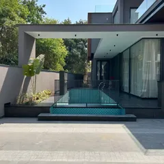 At Gulmohar Farmhouse, the swimming pool is tucked alongside the home, creating a private and accessible aquatic retreat. A simple metal railing provides safety without obstructing the view, and a large canopy offers a shaded area for poolside lounging.