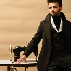 A conceptual shot linking modern menswear with the art of tailoring. The model's sharp, dark suit is juxtaposed with a vintage sewing machine, creating a powerful brand story about craftsmanship.