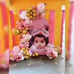 A personalized Annaprashan ceremony backdrop featuring a large photo of the baby. The arched backdrop is framed by an organic balloon garland in pink, rose gold, and white.