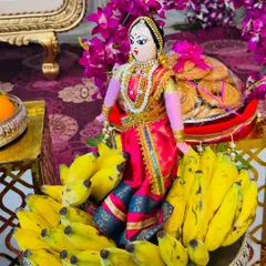 A traditional offering of bananas and sweets, beautifully arranged with a doll dressed in a pink saree. The combination of fresh fruit and decorative elements makes the platter special.
