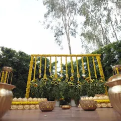 This Haldi decor uses a backdrop of sunflowers and marigold garlands against a lush green setting. The traditional brass urlis (bowls) are filled with flowers, adding an elegant touch.