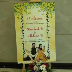 A personalized welcome sign for a wedding reception. The sign features a cute caricature of the couple and is decorated with a fresh flower arrangement at the base.