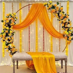 A modern and chic Haldi backdrop featuring a sleek golden ring adorned with yellow and white flowers. The flowing yellow drapes and elegant bench seating create a sophisticated look for indoor or outdoor events.