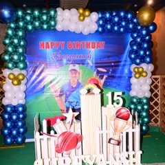 A full view of the cricket-themed birthday party decoration. It includes a large balloon arch, a personalized backdrop with the birthday boy's photo, and marquee letters spelling out his name.