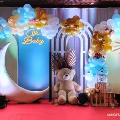 An adorable "Oh Baby" shower setup with a "Twinkle Twinkle Little Star" vibe. It includes a large crescent moon seat, teddy bears, and a blue, white, and gold balloon arch.