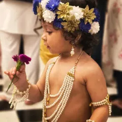 A quiet moment where the child, dressed for Janmashtami, curiously examines a flower. These small, unscripted interactions make for the most memorable and authentic kids' portraits.