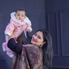 A mother joyfully lifts her baby, who is dressed in a cute pink snowsuit. This candid shot captures a moment of pure happiness and connection.