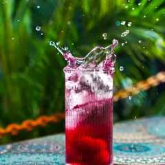 An energetic splash captured in a glass of deep red liquid against a vibrant green, leafy background. This action shot is perfect for conveying a sense of refreshment and excitement for any beverage brand.