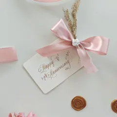A close-up of the elegant "Happy Anniversary" gift tag, featuring delicate calligraphy and adorned with a pink satin ribbon and dried flowers.