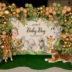 A gorgeous jungle-themed baby shower for a baby boy. The setup features a backdrop with watercolor animals, a balloon frame in sage green and gold, and large stuffed animals like a giraffe and tiger.