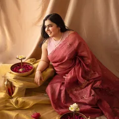 A candid and happy solo portrait of the mother-to-be in her saree, surrounded by traditional decor like brass bowls and flower petals.