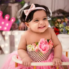 A close-up of a happy one-year-old. Her bright smile and the festive 'ONE' sign in the background perfectly capture the spirit of a first birthday celebration.