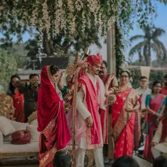 A candid shot from the pheras. The couple circles the sacred fire, their colorful traditional attire vibrant under the daytime sky, surrounded by their loved ones.