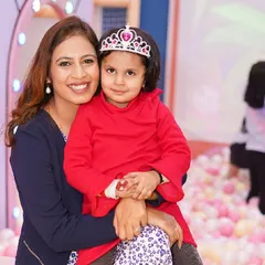 A mother and her daughter, the birthday princess, smile for the camera while sitting in the ball pit.