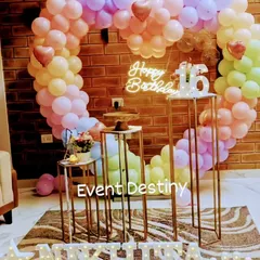 A sweet sixteen birthday setup in a client's home, featuring a large heart-shaped balloon arch in pastel rainbow colors, a custom neon sign, and marquee letters for the name.