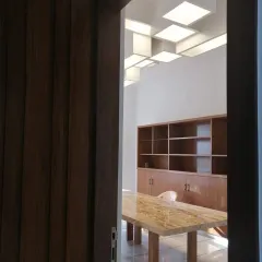 A glimpse into a corporate office we designed, revealing a modern meeting space. The room features a heavy marble table, clean wooden cabinetry, and a custom ceiling light installation, creating a professional and design-forward environment.