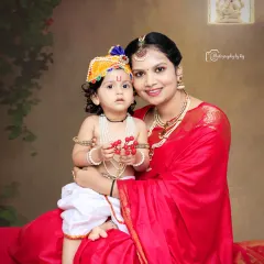 A tender moment between mother and child during our Little Krishna photoshoot. The boy, dressed as Krishna with a pearl necklace and flute, sits comfortably in his mother's lap for a classic, heartfelt portrait.