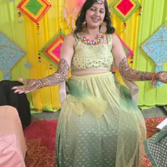 A happy client showing off her full-arm mehandi against a colorful Haldi backdrop. The traditional design is perfect for wedding festivities.