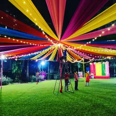 My team setting up the final touches on the large, multi-colored fabric canopy for a dandiya event. The combination of fabric draping and string lights is perfect for evening celebrations in open grounds.