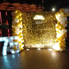 This 75th birthday decoration features a dazzling gold sequin wall. We added simple white and gold balloon columns and a large "75" light-up number to create a focal point that is both elegant and festive.
