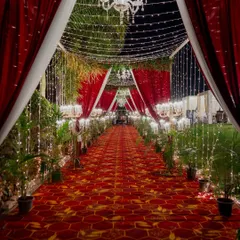 The entrance to a royal affair should be nothing short of majestic. We designed this breathtaking walkway with dramatic red and white drapery, a grand patterned carpet, and a cascade of fairy lights and chandeliers, setting a tone of regal elegance from the very first step.