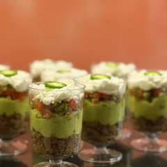 These Mexican Layered Cups are always the life of the party. Each cup is a perfect, individual portion of layered beans, fresh guacamole, zesty salsa, and cool sour cream, finished with a jalapeño kick.