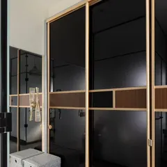 This walk-in dresser features sleek sliding wardrobes with black glass and wood-finish details. The design maximizes storage while maintaining a sophisticated and luxurious feel, connecting seamlessly to the vanity area.