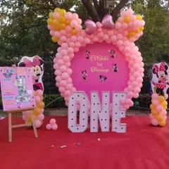 A daytime view of a Minnie Mouse first birthday party. The centerpiece is a balloon frame shaped like Minnie's head, complete with a bow, set against a custom pink backdrop and large marquee "ONE" letters.