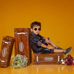 A cool and stylish pre-birthday portrait of a young boy. He is sitting on wooden boxes with sunglasses, posing like a little star for his studio photoshoot.
