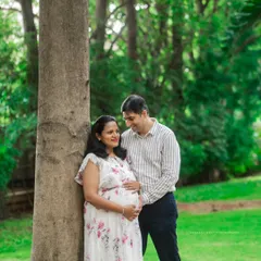 A candid family shot by a tree, capturing a natural and loving interaction between the parents and their daughter during their maternity session.