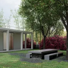 The outdoor living space of the weekend retreat. A simple stone and concrete table and benches sit under the shade of a mature tree, creating a perfect spot for quiet contemplation or a meal with family, fully immersed in the landscape.