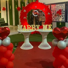 A closer look at a classic proposal setup. The combination of a red balloon arch, a central "Love" neon sign, and glowing "MARRY ME" letters creates a focused and intensely romantic focal point.