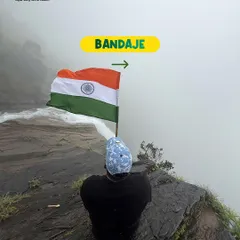 A trekker sits at the edge of a cliff at Bandaje, holding the Indian flag as it billows in the wind.