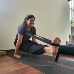 A smile of achievement while working on a challenging pose. This student uses a strap to assist in Brahmacharyasana, finding a balance between effort and ease, which is a core principle of our teaching.