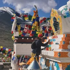 Another angle of me at work on the Stupa. The vibrant colors of the paint stand out against the white structure and the bright blue sky, surrounded by colorful Tibetan prayer flags.
