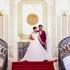 A couple poses on a grand staircase. Our classic white A-line wedding gown gives the bride to be a timeless and regal look.