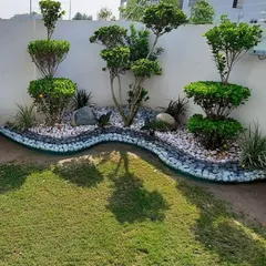 A creative use of a narrow yard space, where we designed a dry riverbed effect using pebbles of different colors. This is bordered by sculpted shrubs and topiary trees to create a highly stylized, low-maintenance garden.