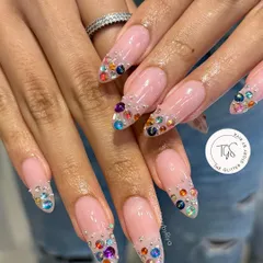 A stunning "crystal pixie" manicure. This design features long, almond-shaped nails with a nude base and tips encrusted with a cascade of colorful, multi-sized crystals.