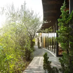 A curved glass wall and wooden walkway follow the natural contours of the landscape at our Himalayan retreat. The design allows the home to sit gently within its environment, surrounded by native trees and plants.
