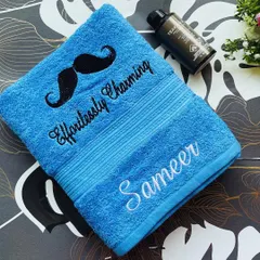 An 'Effortlessly Charming' personalised towel in bright blue, embroidered with a mustache motif and the name 'Sameer'. A great gift for him.