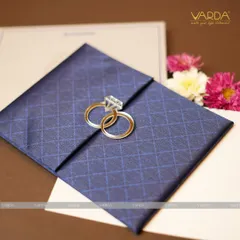 This engagement invitation features a deep blue, diamond-patterned textured folder held together by a unique clasp of two interlocking rings. The design is modern, stylish, and symbolic of the couple's union.