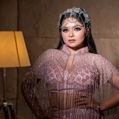 A model posing in a beautiful onion-pink gown with fringe details on the sleeves and a unique headpiece.